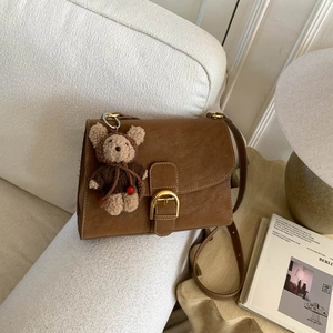 Detalle de bolso vintage marrón con hebilla dorada de herradura y colgante de oso peluche