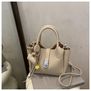 Detalle de bolso de cuero beige con hebilla de reloj plateada y colgante de cara sonriente