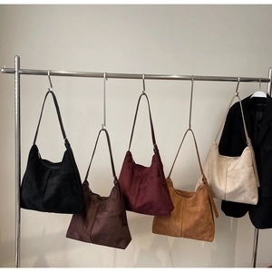 Detail view of five retro suede tote bags in various colors on a modern hanger display