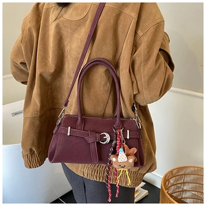 Close-up of retro burgundy matte leather handbag with decorative charms and crossbody strap