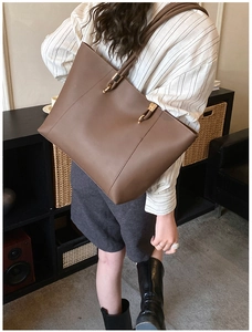 Brown faux leather tote bag with gold hardware and slim straps shown on shoulder