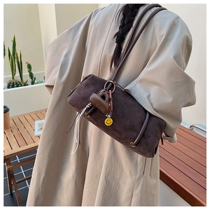 Detail of dark brown suede shoulder bag with heart and smile face pendant on shoulder