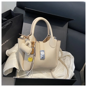 Detalle de bolso de cuero beige con hebilla de metal y colgante de corazón en caja