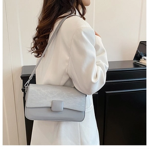 Detail of light blue crossbody bag with textured leather flap on a model in white blazer