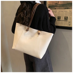 Side view of cream leather tote bag with brown tubular straps on model in stylish interior