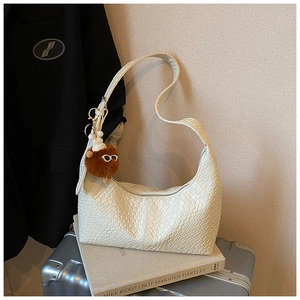 Detail of white woven leather hobo bag with a cute plush charm on a suitcase
