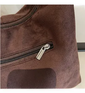 Detail view of smooth silver zipper on a brown suede tote bag with matte texture