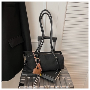 Detail of a large black tote bag with long leather handles on a silver metal suitcase