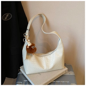 Detail of off-white woven hobo bag with cute plush charm on a textured background