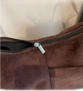 Detailed close-up of the smooth metal zipper and brown suede texture on a crossbody bag