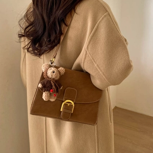 Bolso bandolera de cuero esmerilado marrón con hebilla dorada y peluche en abrigo beige