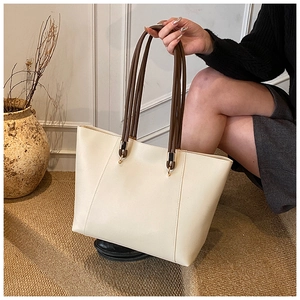 Detail of white faux leather tote bag with brown dual rope handles and gold metal hardware