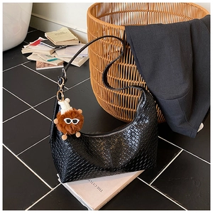 Detail of black woven hobo bag with zip closure and cute plush charm on stone background