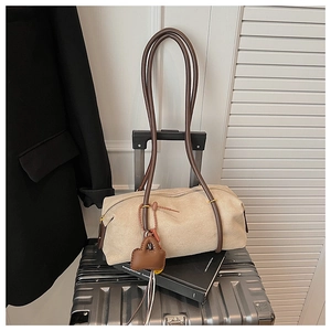 Detailed view of a beige suede cylindrical shoulder bag on a vintage suitcase