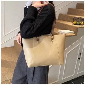 Detail of beige tote bag with dark brown straps and shiny gold metal ring connectors