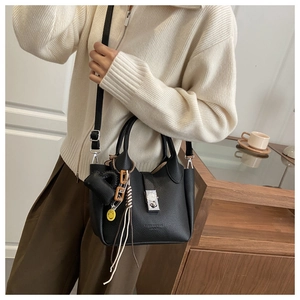 Detalle de bolso de cuero granulado negro con cierre plateado y colgantes usado por una modelo