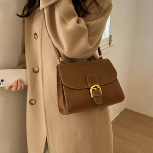 Detalle de bolso cuadrado marrón con hebilla dorada llevado sobre un abrigo de lana beige