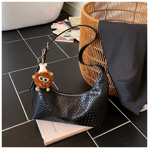 Close-up of black woven hobo bag featuring a cute furry monster charm on white books