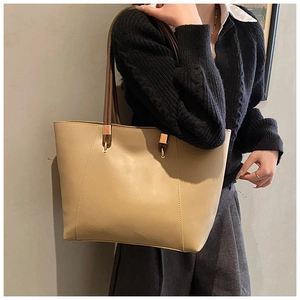 Detail of a large beige tote bag with dark brown handles and elegant gold metal hardware