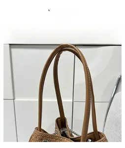 Detail of light brown woven tote bag featuring PU leather handles and metallic chain detail