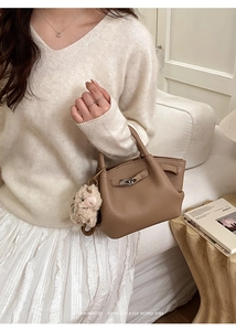 Detailaufnahme der braunen Lederhandtasche mit Lychee-Muster und Plüschschaf-Anhänger