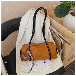 Caramel suede shoulder bag with black handles and charm on a casual lifestyle background
