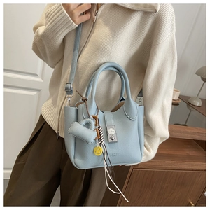 Detalle de bolso de cuero azul claro con cierre de dial y colgante de cara sonriente