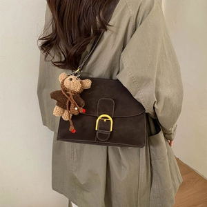 Detalle de bolso bandolera de ante marrón con hebilla dorada y amuleto de oso peluche