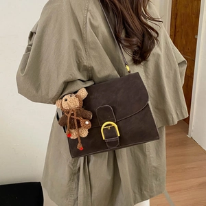 Detalle del bolso retro marrón oscuro con hebilla de herradura dorada y colgante de osito