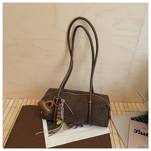 Detail of dark brown suede boston bag with heart charm and tassel on vintage newspaper