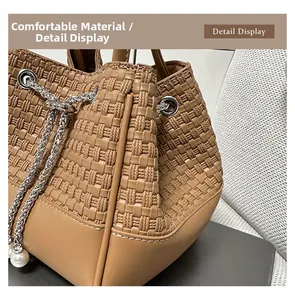 Detail view of woven brown bucket bag featuring silver chain and white pearl drawstring charm