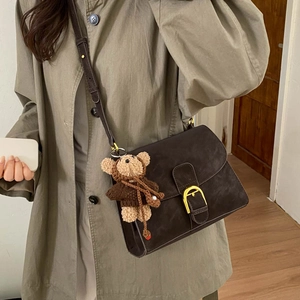 Detalle de bolso retro marrón oscuro con hebilla en D dorada y colgante de osito de peluche
