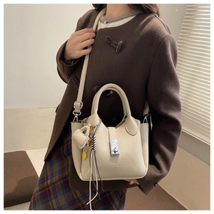 Detalle de bolso crema con textura de lichi, cierre giratorio y colgante de corazón
