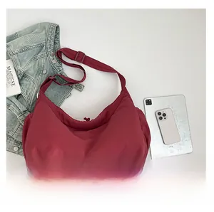 Detail view of spacious burgundy nylon half-moon shoulder bag next to an iPad for scale