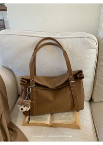 Détail du sac bandoulière rétro marron avec breloque ours sur un canapé beige