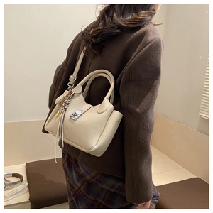 Detalle de bolso tipo cesta blanco crema con cierre plateado y borla usado por una modelo