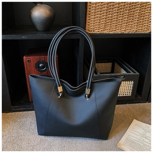 Close-up of black leather tote bag featuring golden metal rings and triple strap detail