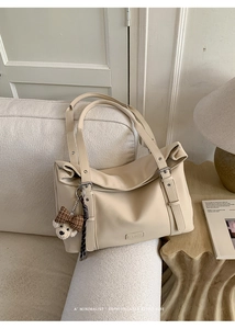 Détail du sac cabas blanc crème avec pendentif ours sur un canapé en tissu beige