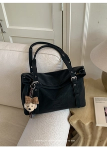 Détail d'un grand sac à bandoulière noir avec un pendentif peluche chiot sur un canapé