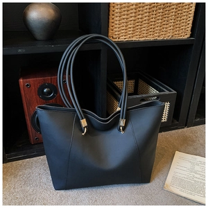 Detail of black leather tote bag with sturdy gold metal hardware and long shoulder handles