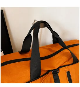 Detail of orange travel bag featuring black nylon handles and durable metal D-ring attachment
