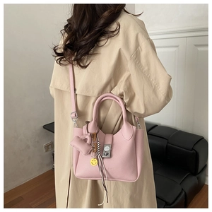 Bolso tipo cubo en cuero rosa con hebilla de reloj y colgantes decorativos sobre una gabardina
