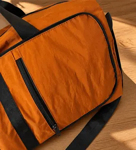 Detailed view of orange nylon travel bag with black zippers and durable woven straps