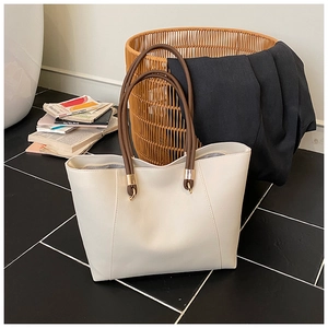 Detail of cream tote bag featuring brown handles and gold hardware in a lifestyle setting