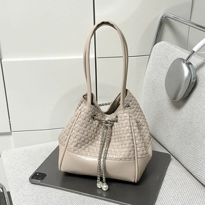 Détail du sac seau beige tressé avec cordon argenté et pendentifs en perles