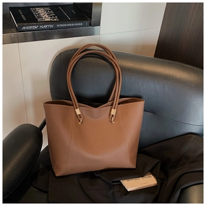 Close-up of brown leather tote bag with gold metal hardware on a classic sofa