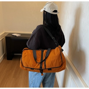 Detail of a large orange travel duffel bag showing durable nylon material and shoulder strap