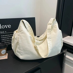 Close-up of cream nylon dumpling bag with adjustable wide strap on a minimalist display