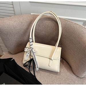 Detail of cream leather shoulder bag with embossed logo and elegant ribbon charm