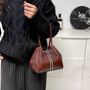 Détail d'un sac seau marron tressé avec cordon en chaîne argentée et perles blanches